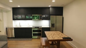 A compact kitchen with dark cabinets, stainless steel appliances, and a wooden table with a woven mat. - The Wooded Retreat (McLean)