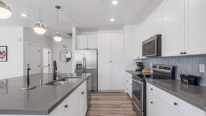 A modern kitchen with white cabinets, stainless steel appliances, and a large island with a sink. - Vintage Desert 5 BDR w/ Resort Amenities (Hurricane)