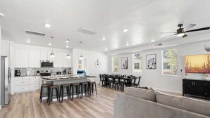 A spacious kitchen with white cabinets, a central island with stools, and a dining area with a black table and chairs. - Vintage Desert 5 BDR w/ Resort Amenities (Hurricane)