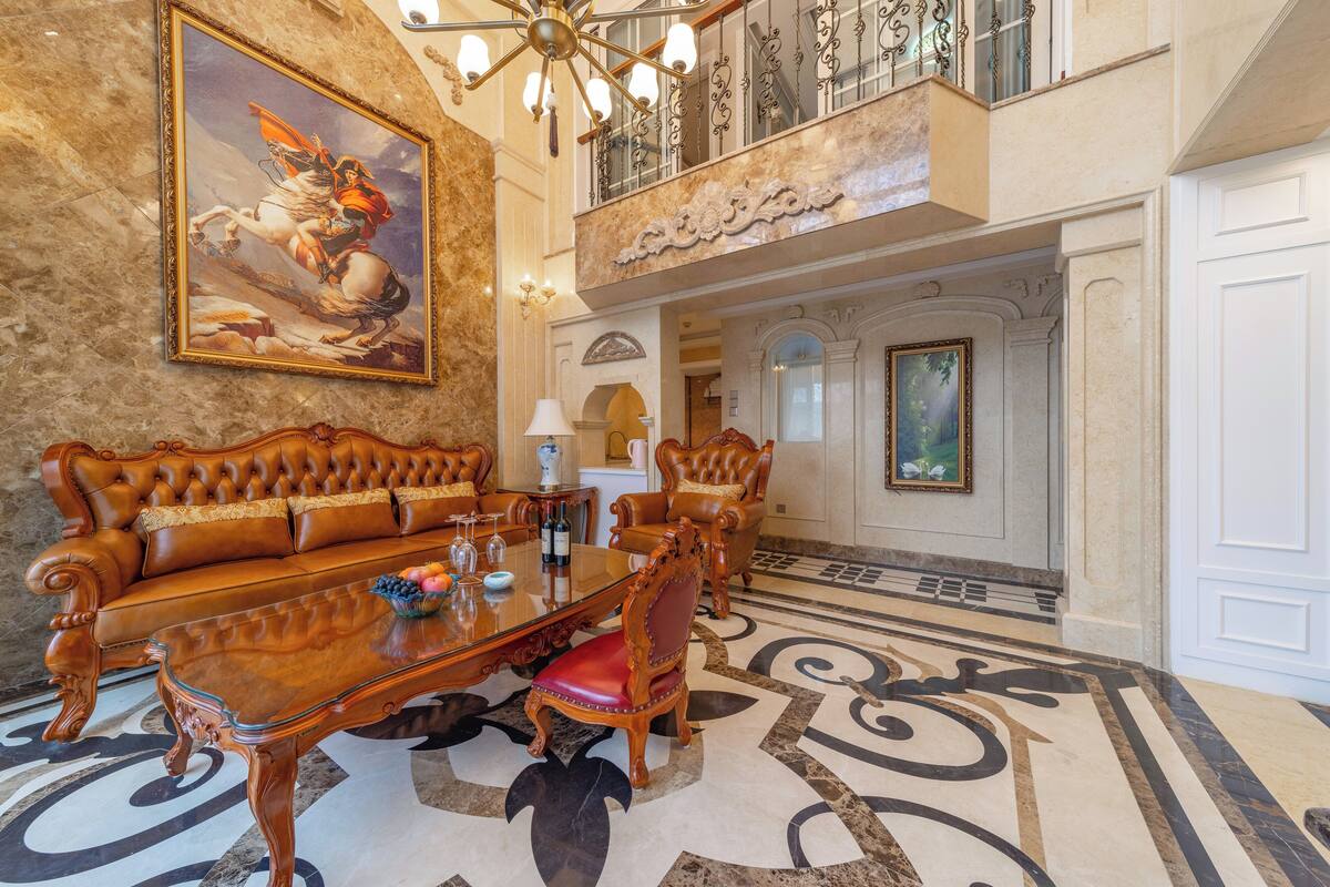 A grand lobby with a marble floor, a large painting, a chandelier, and a seating area with a table and chairs.