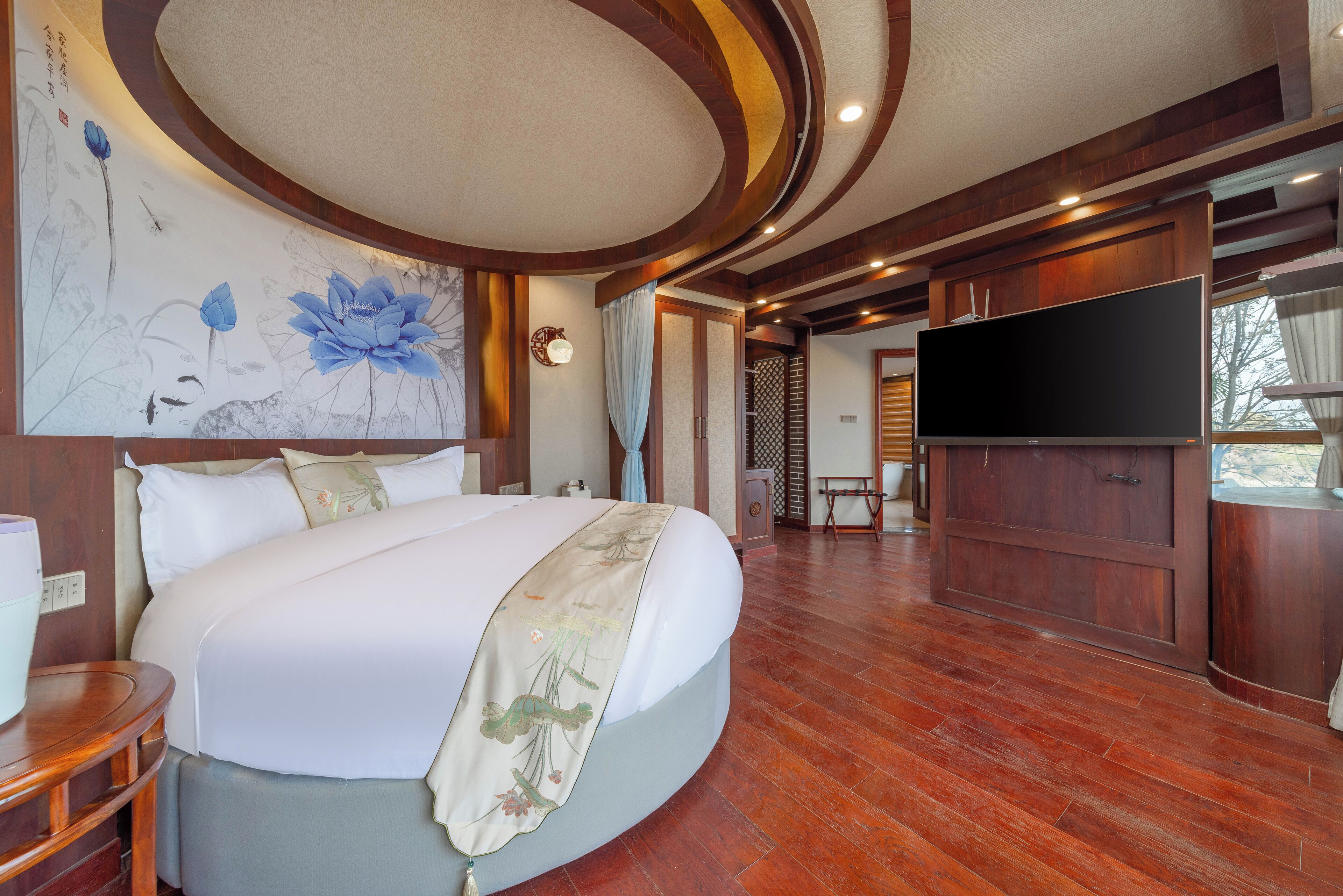 A spacious bedroom with a large bed, a flat-screen TV, wooden flooring, and a decorative wall mural.