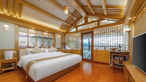 A spacious bedroom with a large bed, wooden flooring, a view of the outdoors, and a sliding door leading to a balcony. - Cloudhaven Retreat (花开花落半山居) (Lijiang)