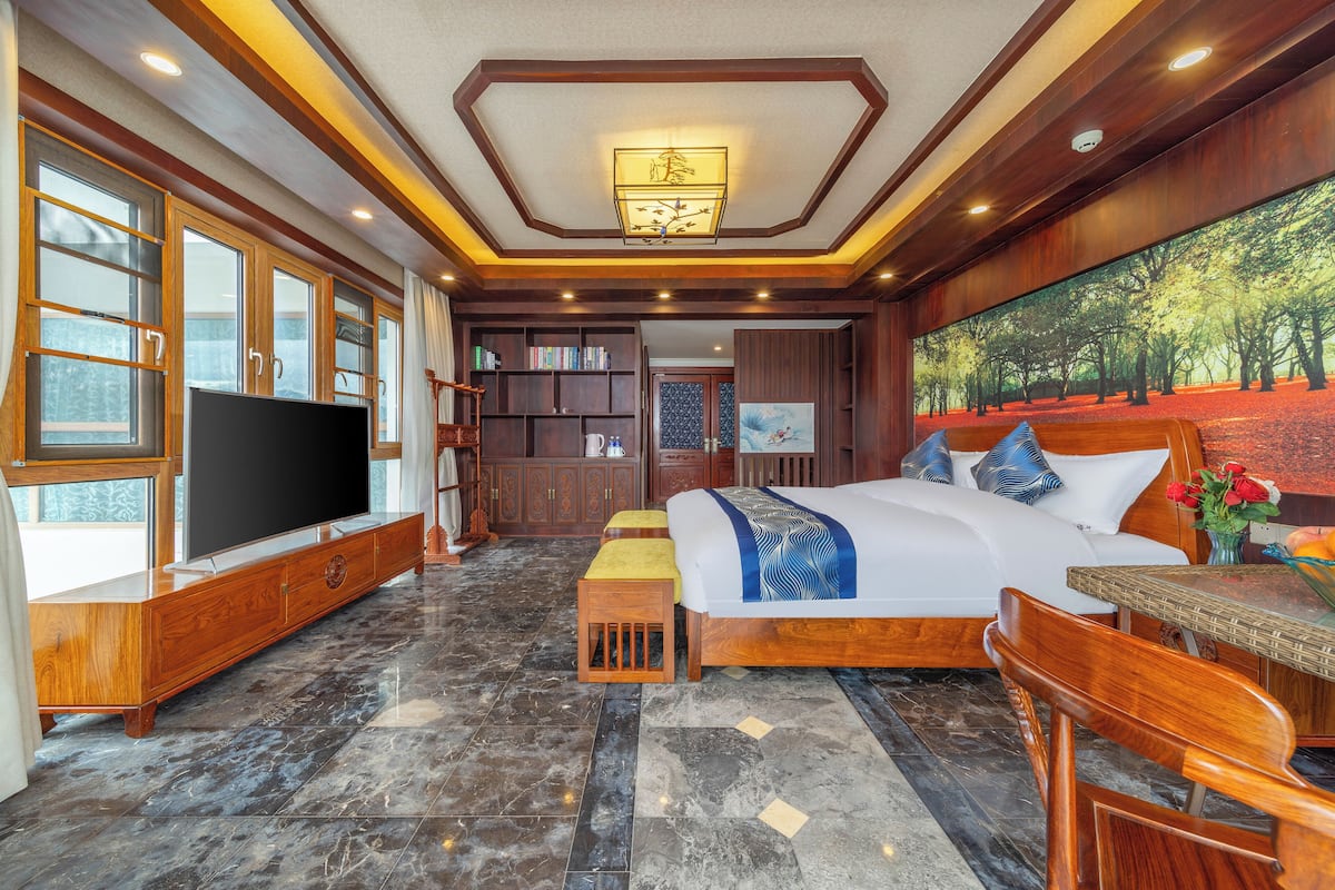 A spacious bedroom with a large bed, wooden furniture, a flat-screen TV, and a painting on the wall.