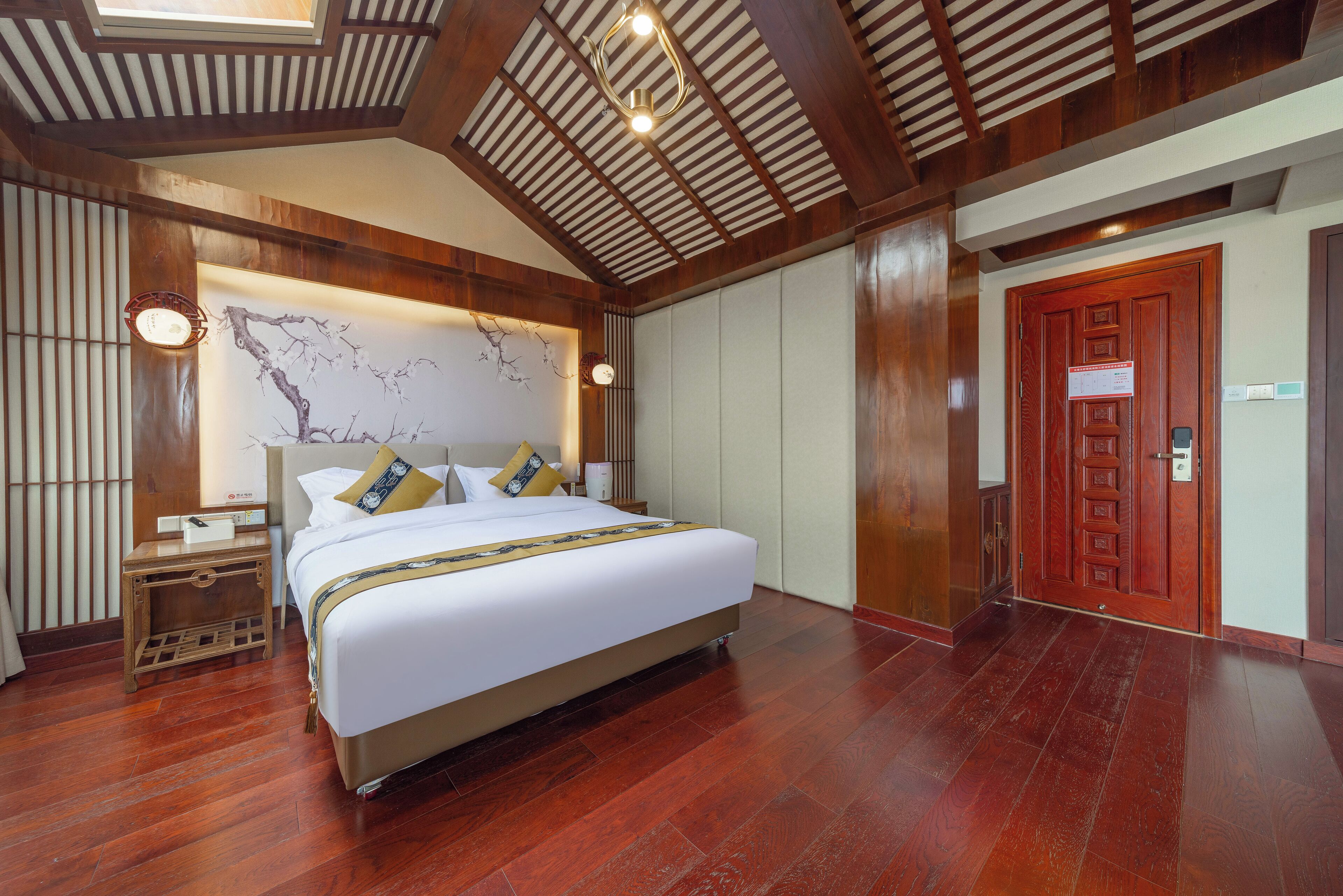 A hotel room with a large bed, wooden flooring, a ceiling with wooden beams, and a wall-mounted clock.