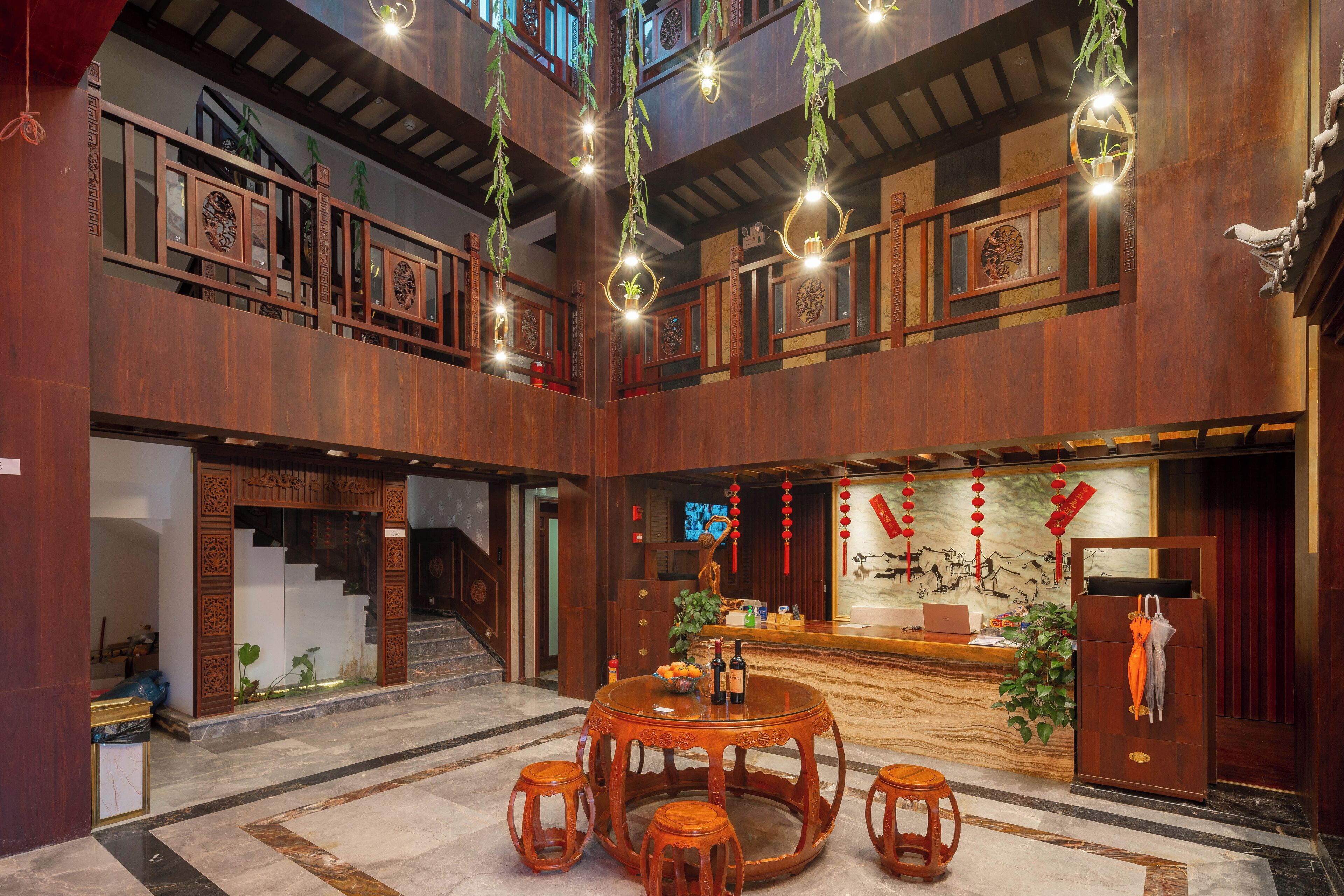A traditional wooden interior with a central round table and stools, a reception desk, and a staircase.