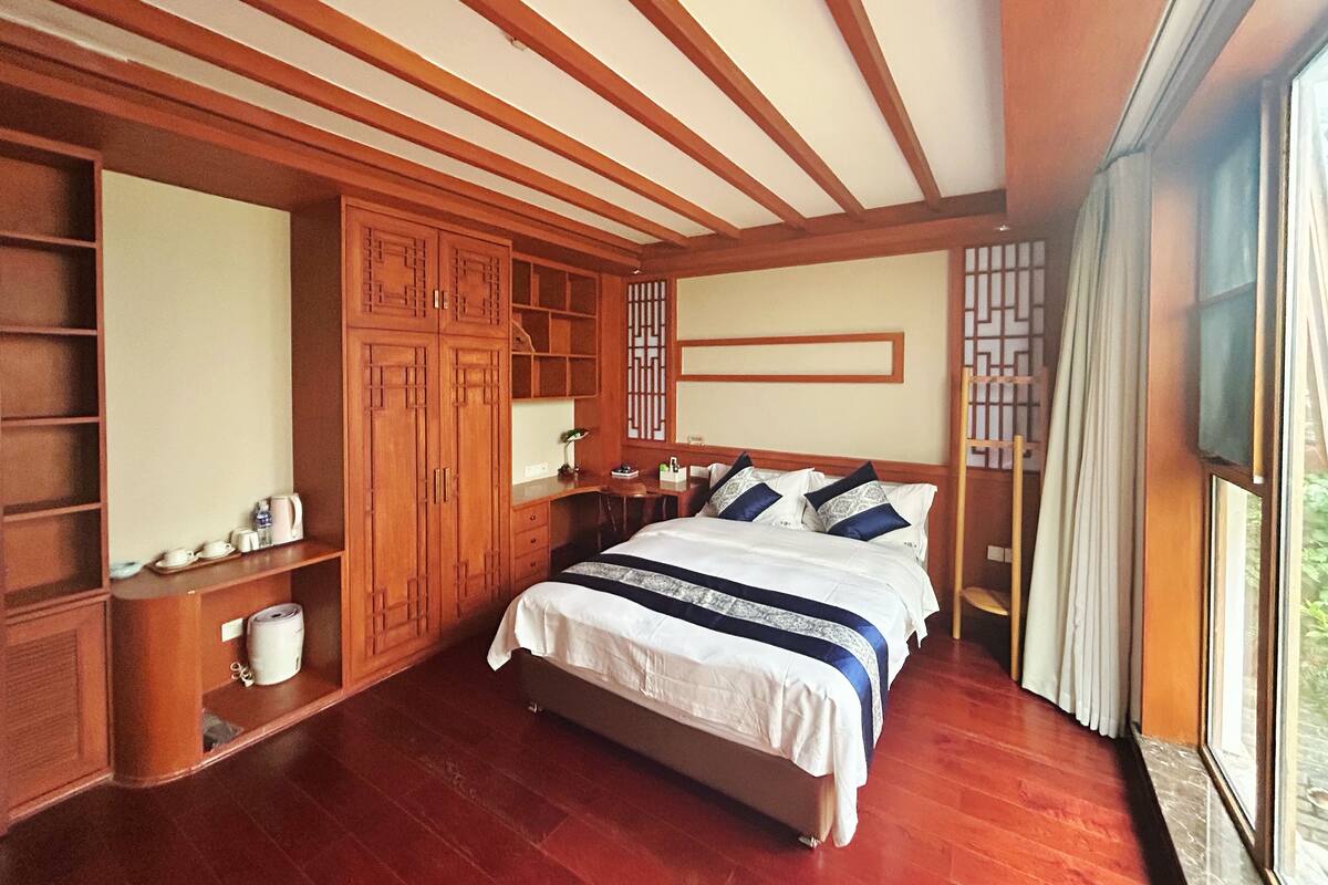 A bedroom with a large bed, wooden wardrobe, and a desk.