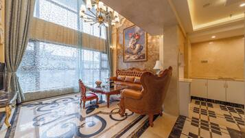 A luxurious living room with a sofa, coffee table, and chairs, a chandelier, and a large window with curtains.
