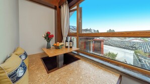 A corner room with a wooden bench, a small table with a vase of flowers, and a view of traditional buildings through a large window. - Cloudhaven Retreat (花开花落半山居) (Lijiang)