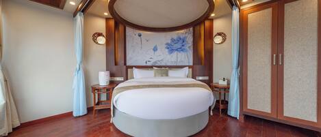 A circular bed with a headboard, wooden flooring, and a ceiling with recessed lighting.