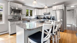 A modern kitchen with white cabinetry, stainless steel appliances, and a central island with bar stools. - Maine Adventure 3BR Oasis Awaits! (York)