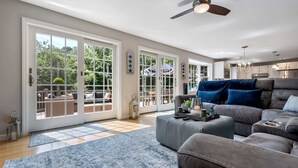 A spacious living room with a large grey sofa, a blue patterned rug, and a ceiling fan. - Maine Adventure 3BR Oasis Awaits! (York)