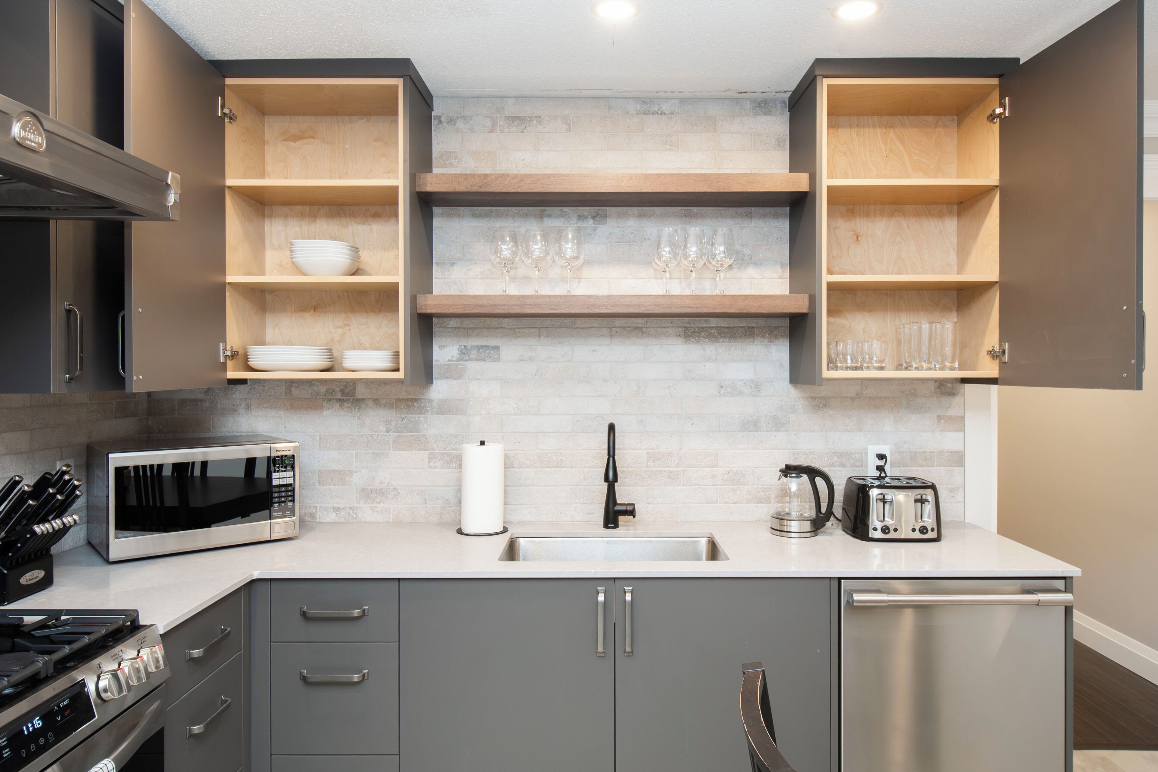 A modern kitchen with a built-in microwave, stainless steel appliances, and wooden shelves.