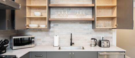 A modern kitchen with a built-in microwave, stainless steel appliances, and wooden shelves.