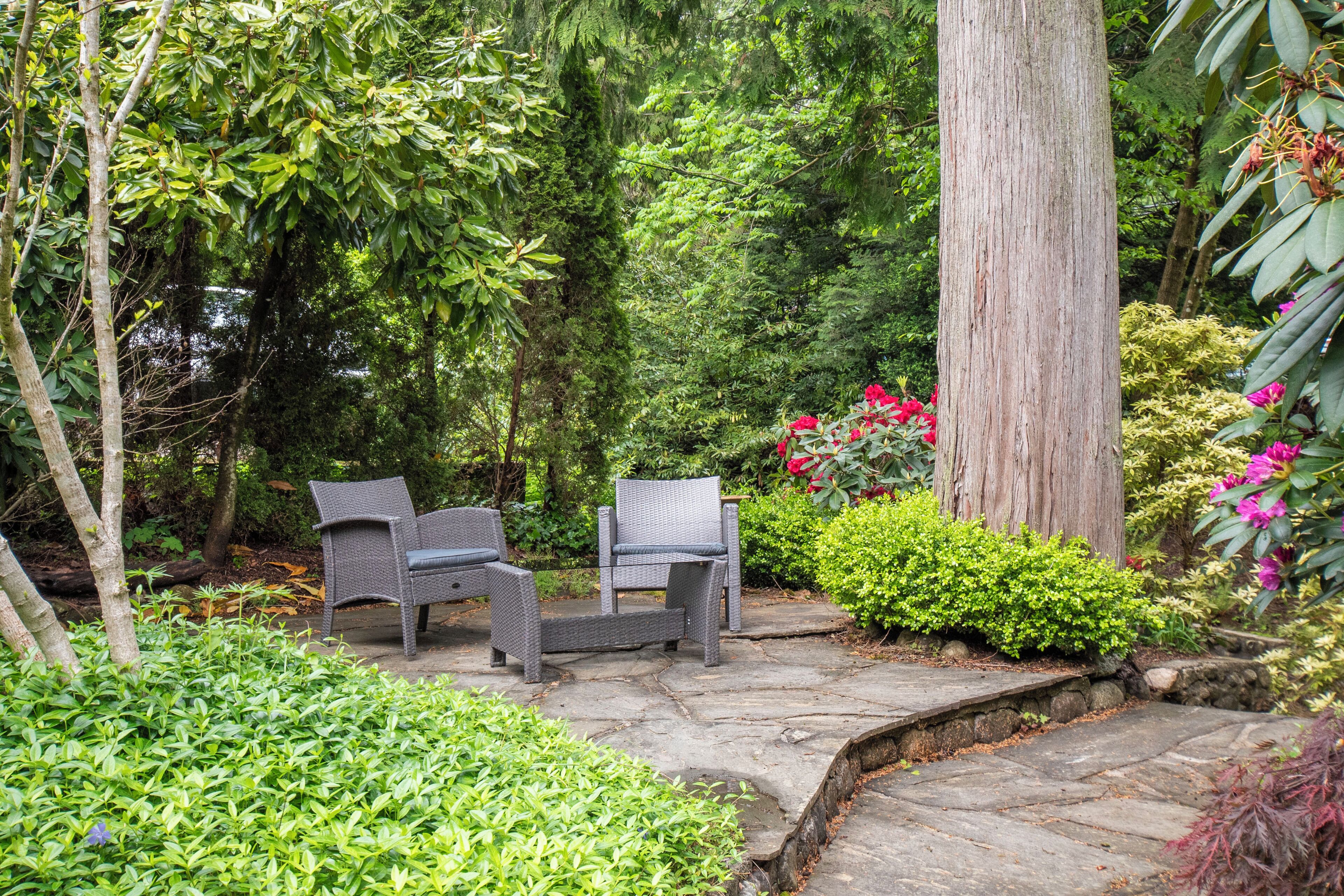 A garden with stone pathways, wicker furniture, and lush greenery.