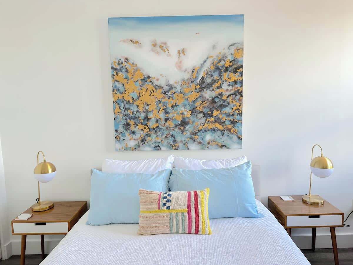 Une chambre à coucher avec un lit, deux tables de chevet et un tableau accroché au mur.