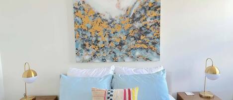 Une chambre à coucher avec un lit, deux tables de chevet et un tableau accroché au mur.