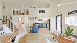 Una cocina amplia con una isla central, un comedor con mesa de madera y una escalera que sube a un nivel superior.