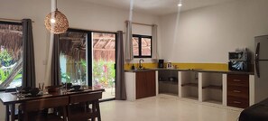 A modern kitchen with a dining area, large windows, and a view of greenery.