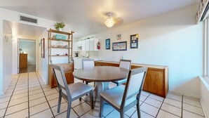 Un coin repas avec une table ronde, quatre chaises, une bibliothèque et, au fond, une cuisine.