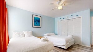 Une chambre d’hôtel avec deux lits, un ventilateur de plafond, un tableau encadré au mur et un placard avec des portes à persiennes.