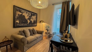 Una sala de estar moderna con un sofá gris, una obra de arte con un mapa del mundo, una lámpara colgante original, una mesa de comedor con una botella de vino y un televisor de pantalla plana montado en la pared.