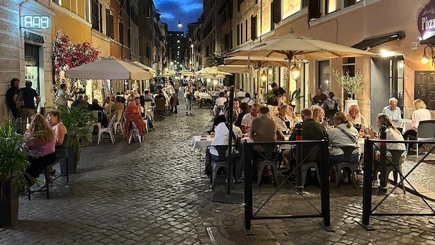 Una calle empedrada bordeada de cafés y restaurantes, con gente comiendo y caminando.