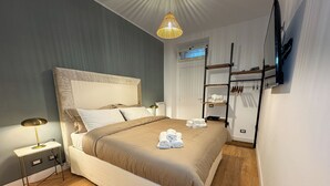 Un dormitorio ordenado con una cama grande, mesitas de noche, una lámpara colgante, un zapatero y un televisor de pantalla plana montado en la pared.