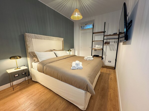 Un dormitorio ordenado con una cama grande, mesitas de noche, una lámpara colgante, un zapatero y un televisor de pantalla plana montado en la pared.
