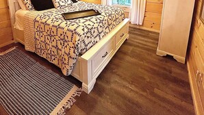 A bedroom with a bed, a ceiling fan, a dresser, and a window with curtains.