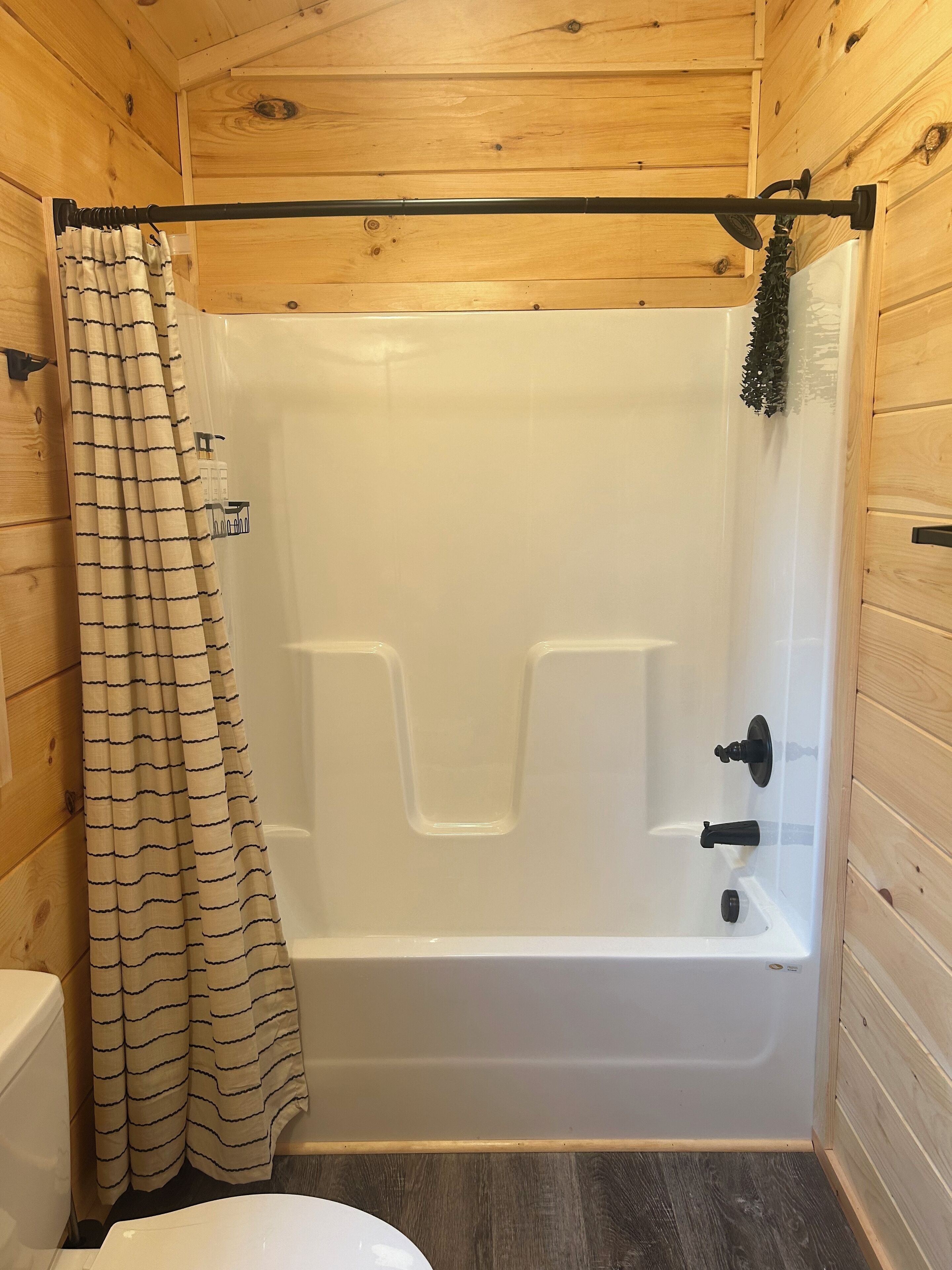 Een badkamer met houten lambrisering, een witte badkuip, een badgordijn met strepen en een klein plankje met toiletartikelen.