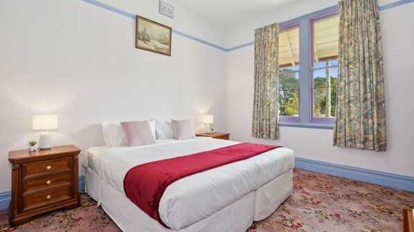 A bedroom with a bed, two bedside tables, a nightstand, a window with curtains, and a framed picture on the wall. - The Outlook in Leura (Leura)