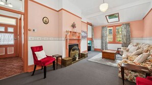 A living room with a fireplace, a red armchair, a floral sofa, and a wooden coffee table. - The Outlook in Leura (Leura)