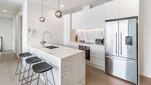 Una cocina moderna con armarios blancos, una isla de mármol, electrodomésticos de acero inoxidable y taburetes negros.