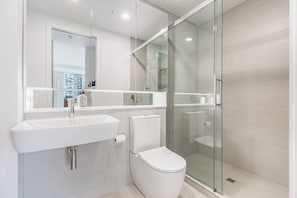 Un baño moderno con cabina de ducha de vidrio, un lavabo blanco y un inodoro.