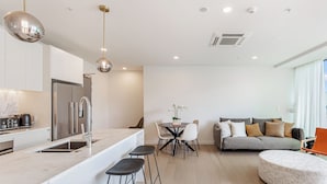 Una cocina moderna con una isla central, un área de comedor con una mesa redonda y sillas, un sofá gris y un otoman redondo.