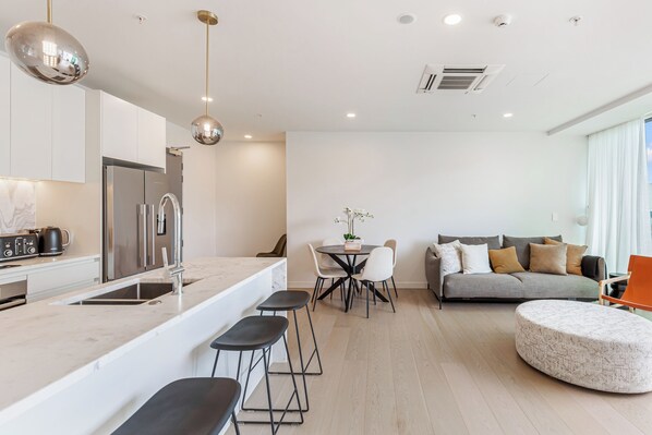 Una cocina moderna con una isla central, un área de comedor con una mesa redonda y sillas, un sofá gris y un otoman redondo.