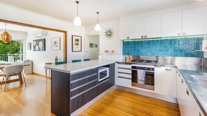 A modern kitchen with white cabinets, a central island, and a blue backsplash. - Spacious 3Br Mission Bay Home With Parking! (Auckland)
