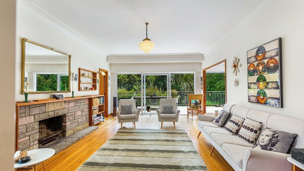 A spacious living room with a fireplace, a sofa set, and a large window offering a view of greenery. - Spacious 3Br Mission Bay Home With Parking! (Auckland)