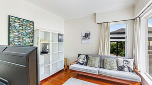 A living room with a sofa, a television, a bookshelf, and a window with curtains. - Spacious 3Br Mission Bay Home With Parking! (Auckland)