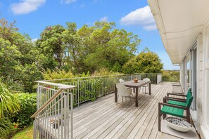 A wooden deck with a table and chairs, surrounded by lush greenery and a white railing. - Spacious 3Br Mission Bay Home With Parking! (Auckland)