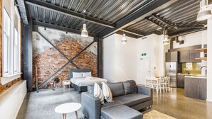 Un interior moderno con pared de ladrillo, sofás grises, una mesita redonda y una zona de cocina.