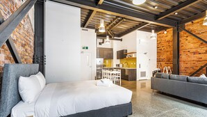 Una habitación de hotel moderna con una cama grande, un sofá, una zona de cocina y paredes de ladrillo visto.