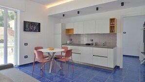 A modern kitchen with white cabinets, a blue tiled floor, and a dining area with pink chairs. - The Bell Tower Clock vacation home (Minori)