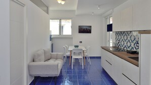 A modern kitchen with white cabinets, a tiled backsplash, and a dining area with a white table and chairs. - The Bell Tower Clock vacation home (Minori)