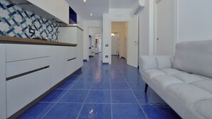 A hallway with a blue tiled floor, white walls, and a white sofa. - The Bell Tower Clock vacation home (Minori)