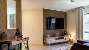 Ein modernes Wohnzimmer mit einem an der Wand befestigten Flachbildfernseher, einem Holztisch, einer Couch und einem gemusterten Teppich.