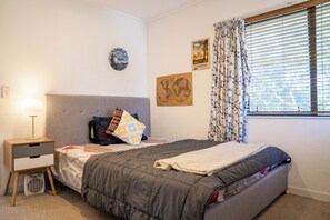 Une chambre à coucher avec un lit, une table de chevet, une lampe, une horloge murale et une fenêtre avec des rideaux.