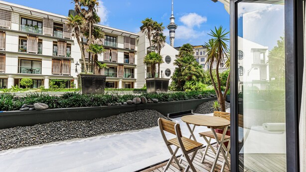 Un patio de hotel moderno con mobiliario exterior, vistas a una torre y jardines exuberantes.