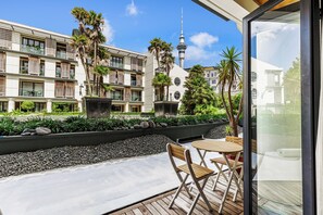 Ein moderner Hotelinnenhof mit Außenbestuhlung, Blick auf einen Turm und üppiger Bepflanzung.