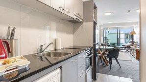 A modern kitchen with stainless steel appliances, a dishwasher, and a dining area with a table and chairs. - Zodiak Stays: Cozy CBD 2BR Near Top Dining Spots (Auckland)